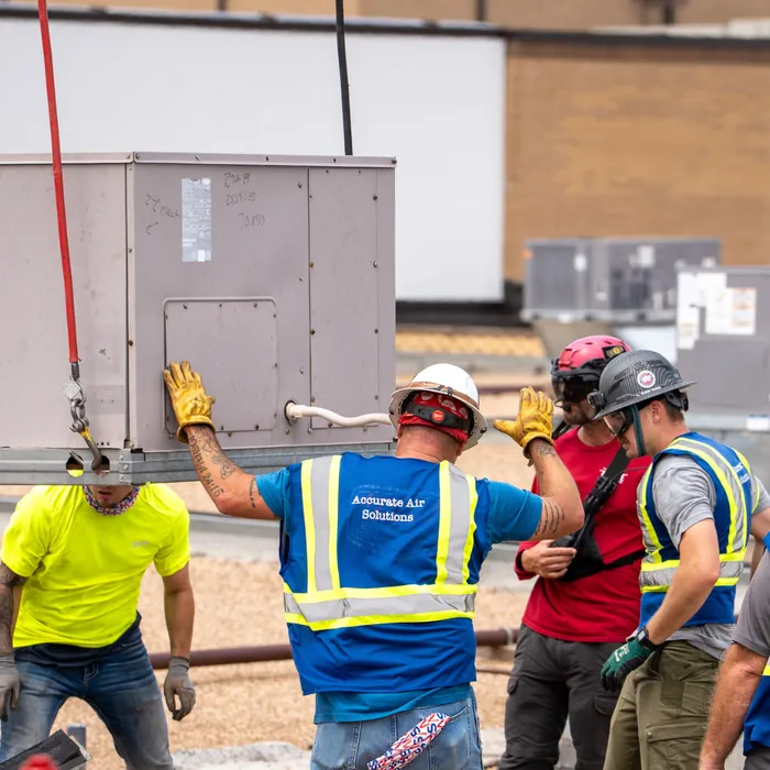 Crew rigging and tag-lining a rooftop unit in full PPE